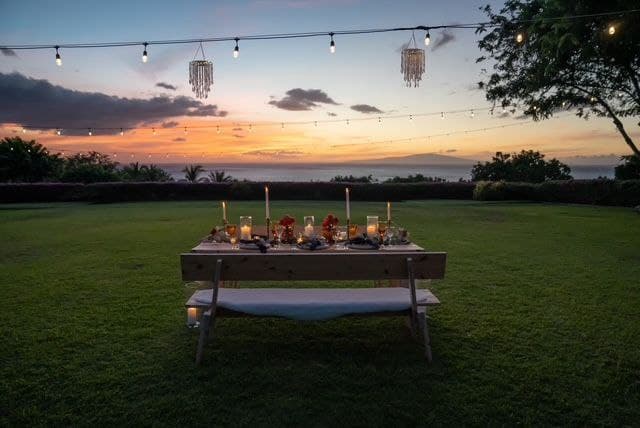 Intimate Maui wedding dinner table at sunset with string lights and candles on a lush green lawn