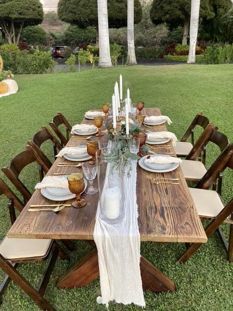 Rustic farm table wedding reception with amber glasses, candles, and cheesecloth runner on Maui lawn